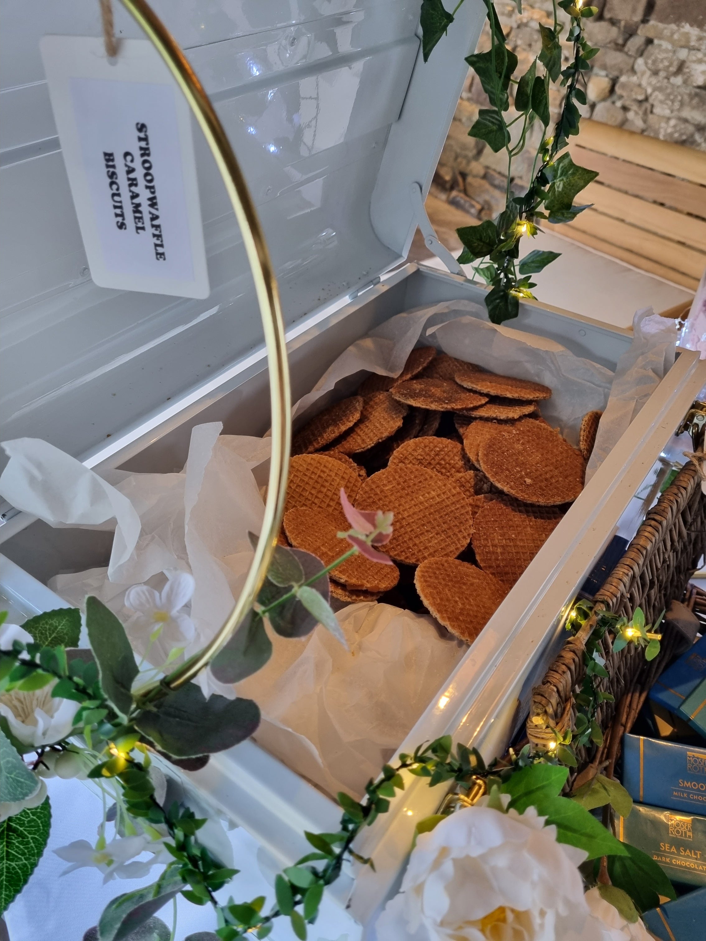 Open box containing stroopwaffle caramel cookies with decorative elements and a tag on top of a smores staion at healey barn wedding venue in northumberland