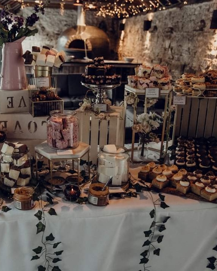 Dessert table with various baked treats and marshmallows table against a brick wall background at healey barn wedding venue