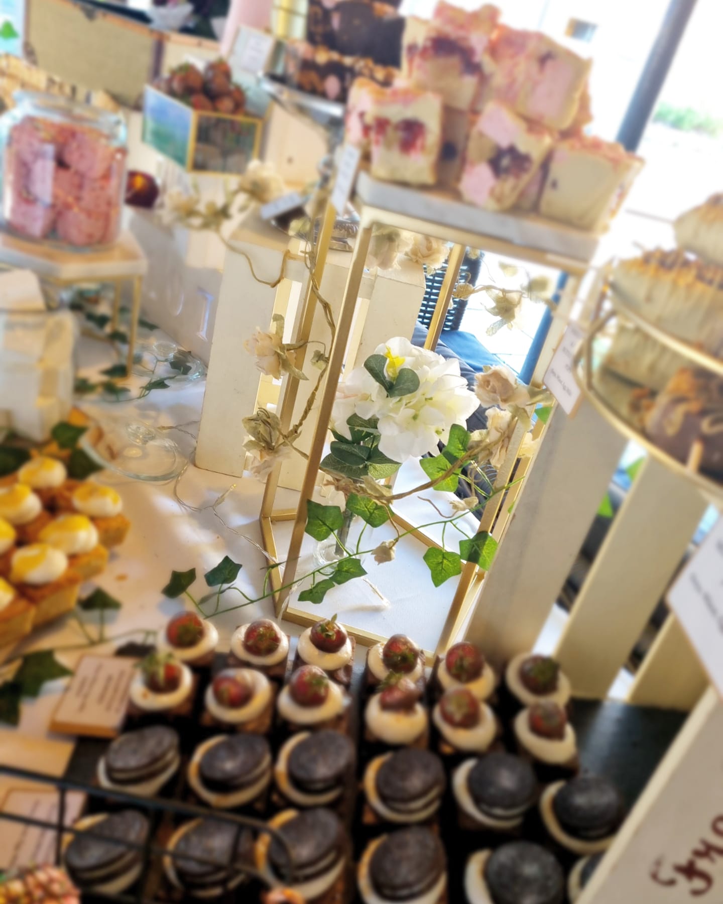 Decorative cake stand with assorted baked treats including cupcakes and tarts on a dessert table at healey barn wedding venue