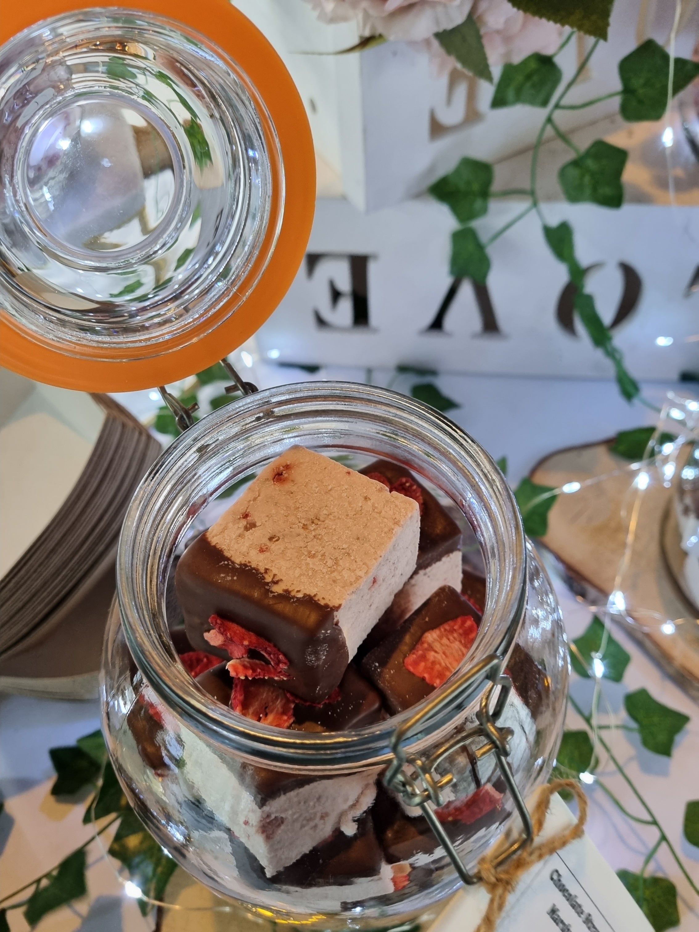Jar of chocolate-dipped marshmallow with a decorative greenery background.