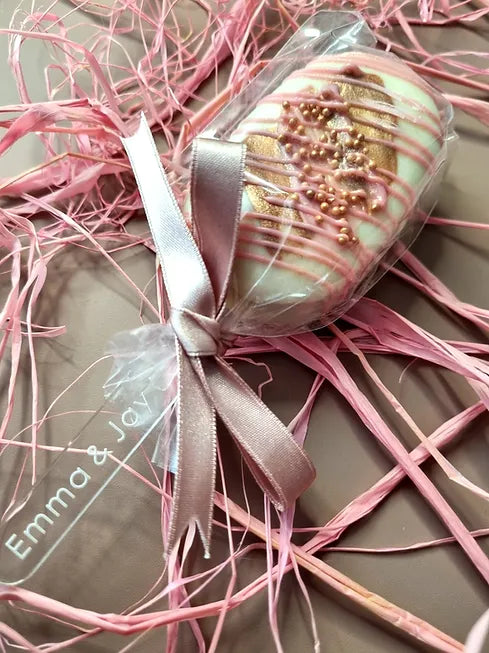 Decorative chocolate item with pink ribbon and gold accents on a brown surface wedding favour