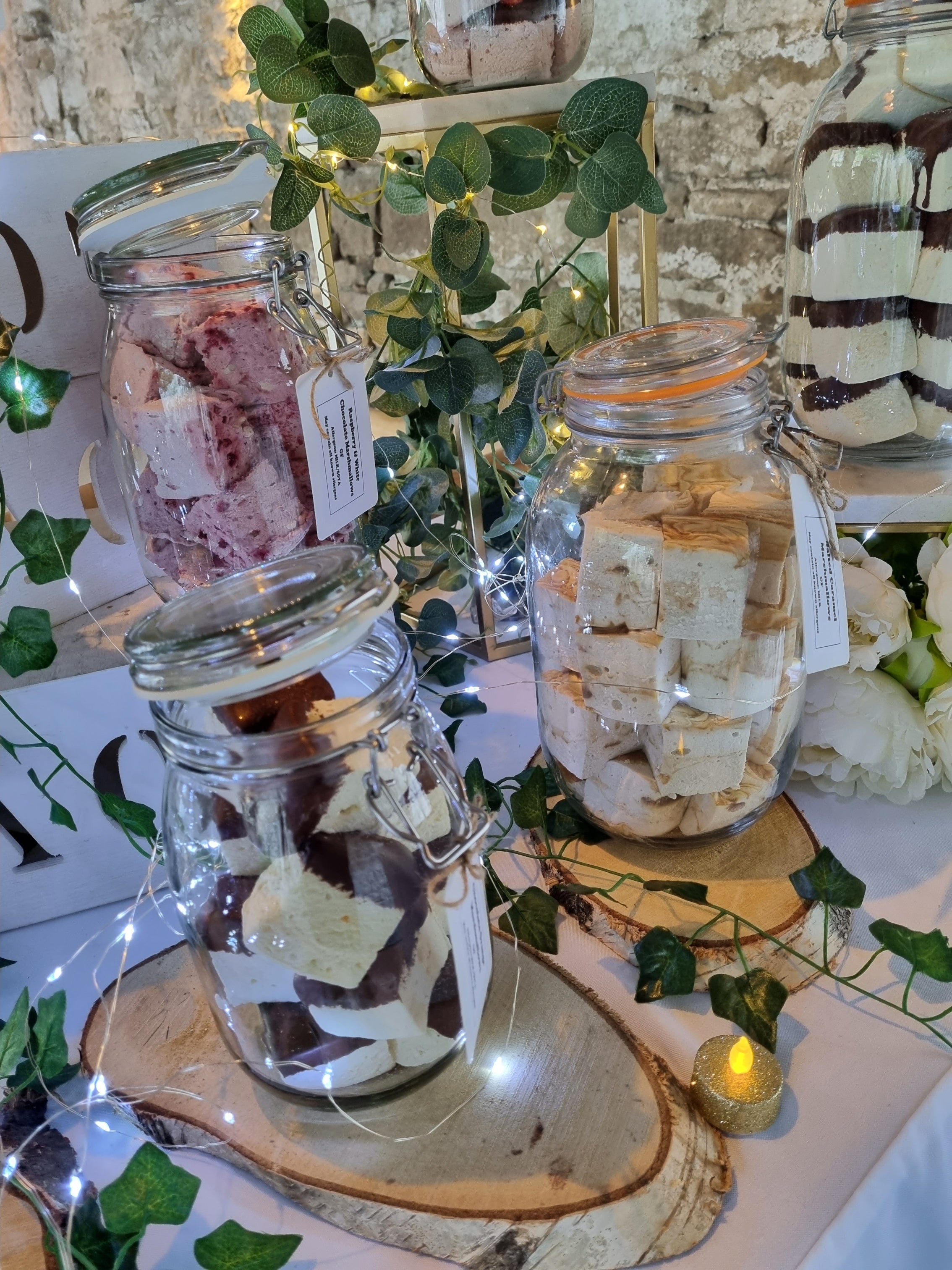 Decorative setup with glass jars containing treats on a smores table with greenery and candles.