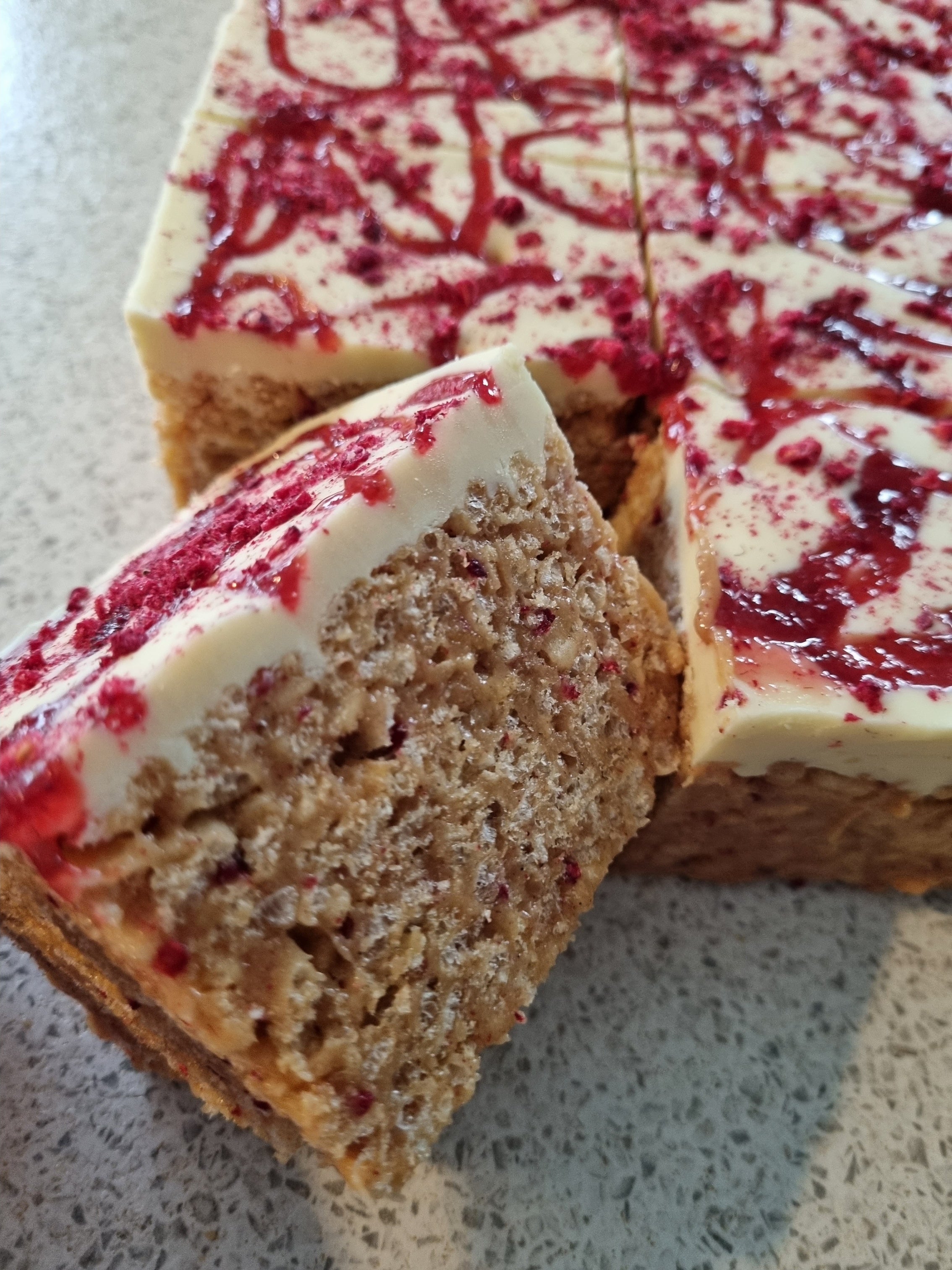 Slice of rice crispie treats with red jelly swirls on a textured surface