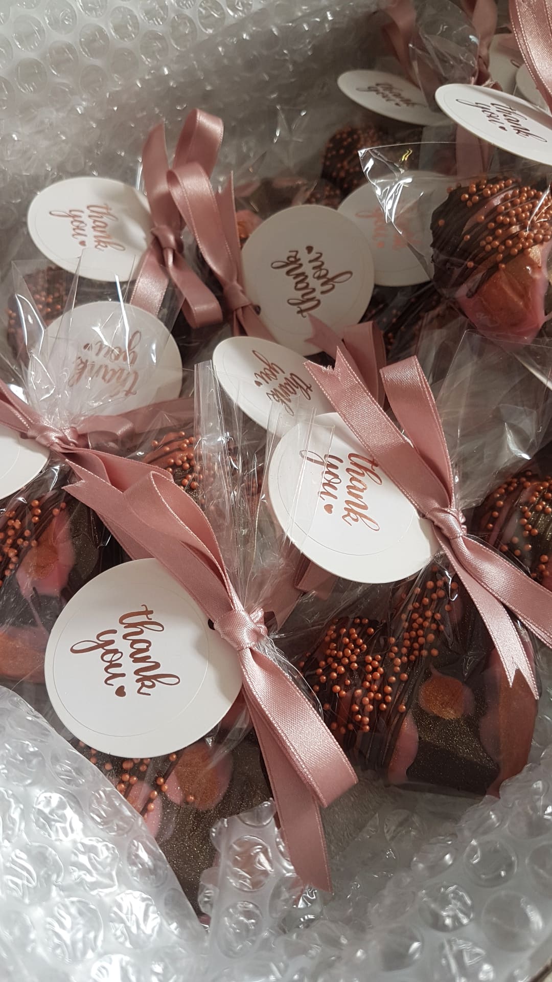 Chocolate geo hearts wrapped in cellophane and tied with pink ribbons and 'thank you' tags on a bubble wrap background in a packing box