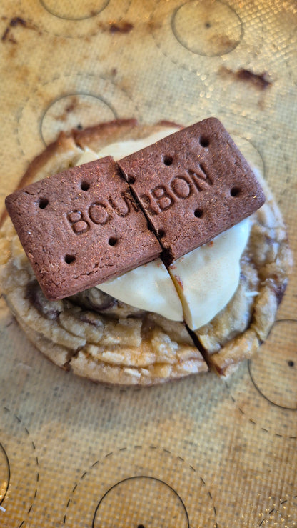 Two halves of chocolate chip cookie with a white chocolate drizzle and bourbon biscuit top on a wooden surface