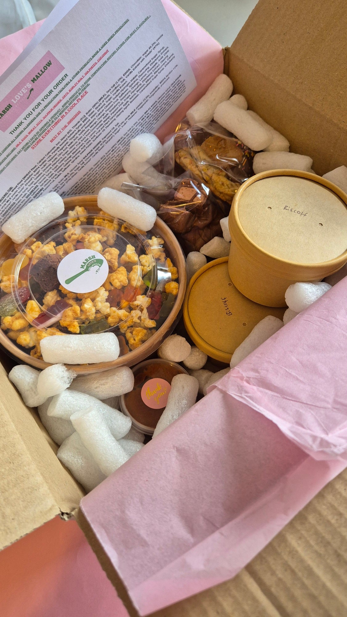 Box containing snacks and fluff pots with packing peanuts around them. with pink tissue paper.