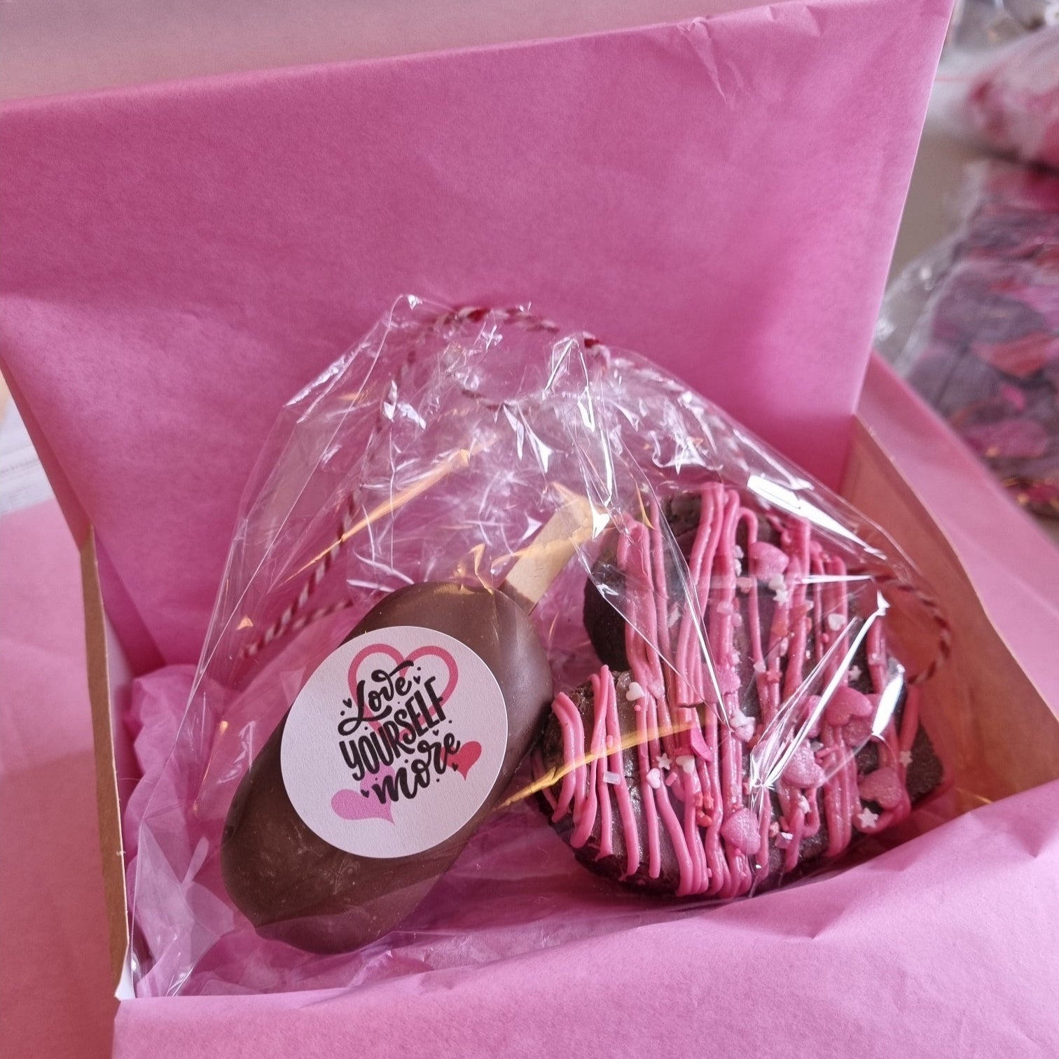 Bouquet of pink and chocolate cookies with a 'Love Yourself More' sticker in a pink box.
