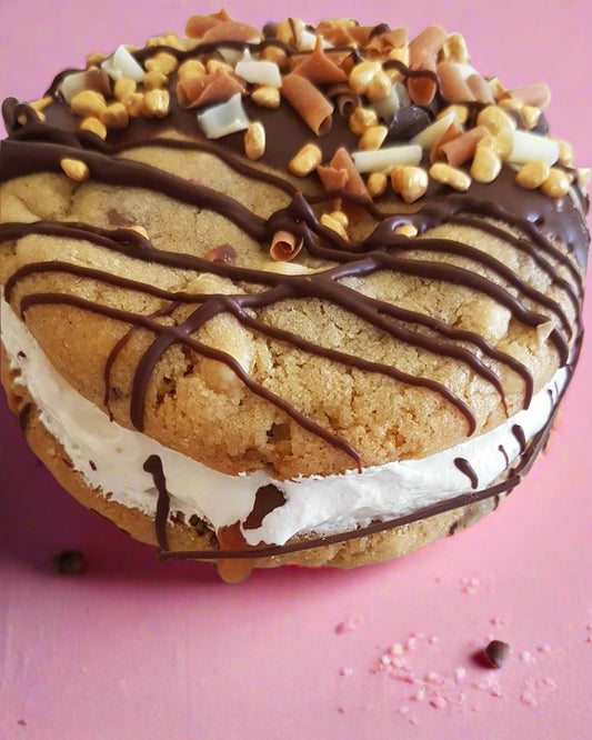A Cookie Fluff Sandwich filled with marshmallow fluff & salted caramel sauce. Drizzled in chocolate & finished with sprinkles.