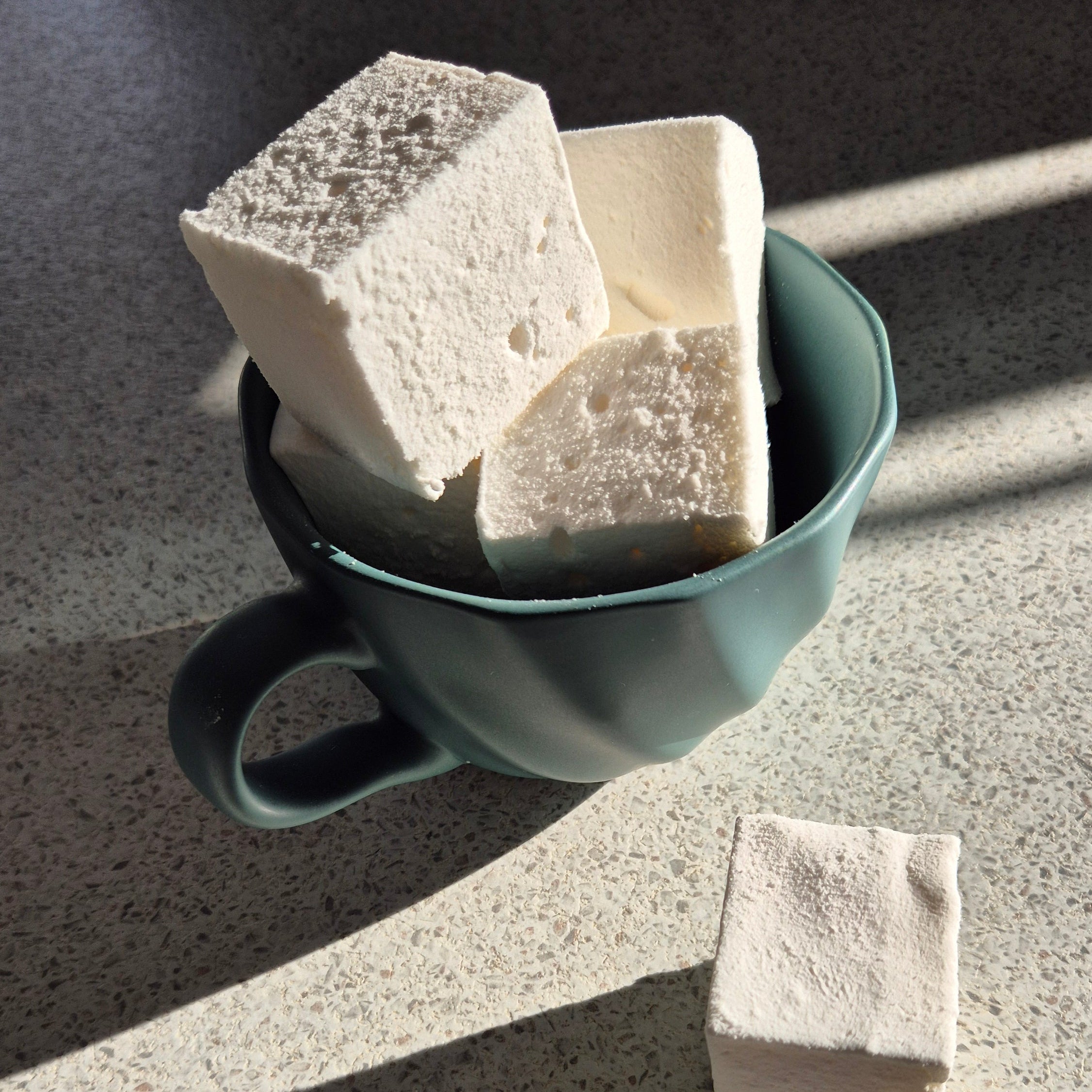 Green ceramic cup with three stone-like blocks on a textured surface