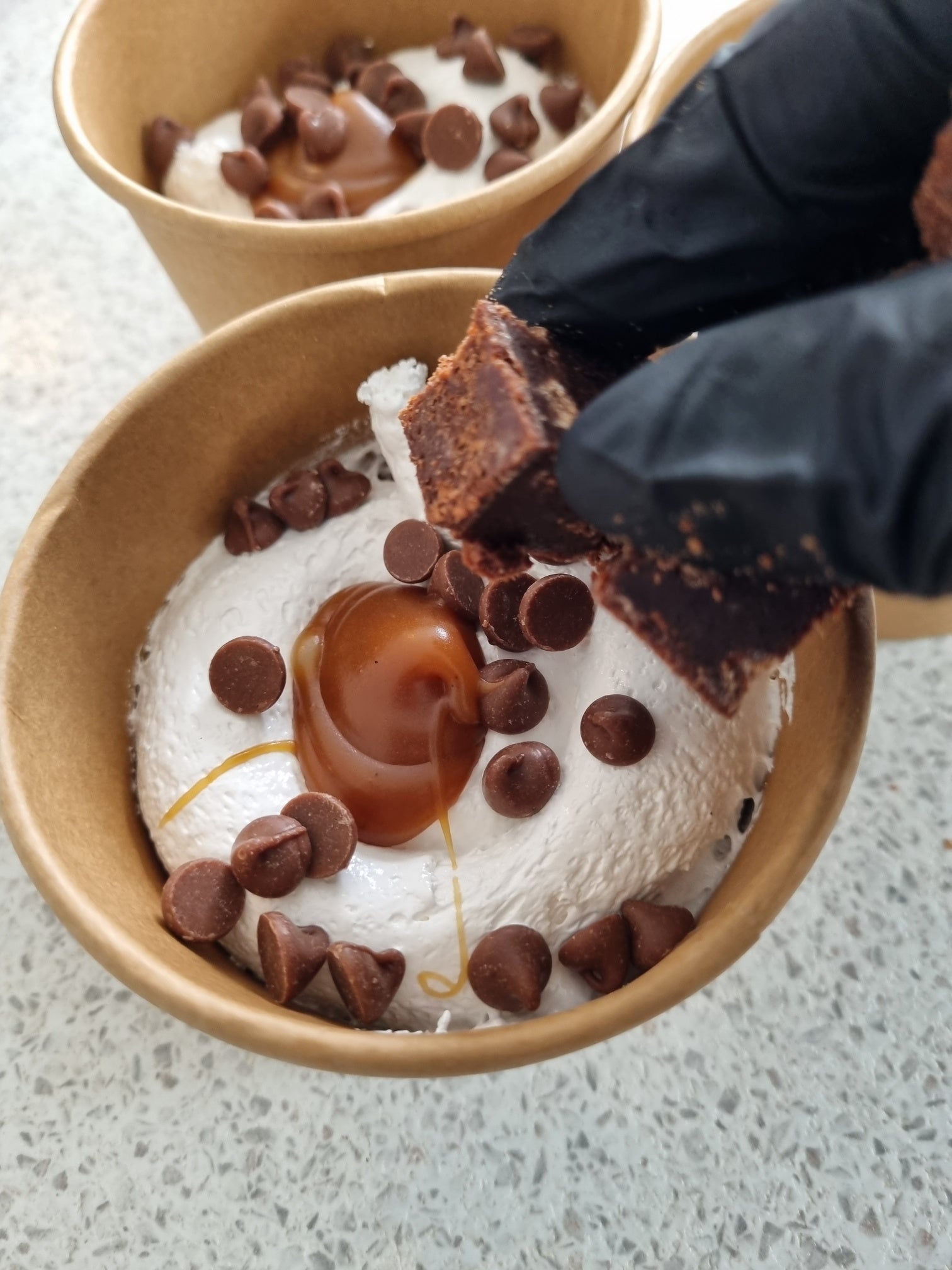 Dessert bowl with  marshmallow fluff, chocolate chips, and a brownie piece being added by the marsh loves mallow owner