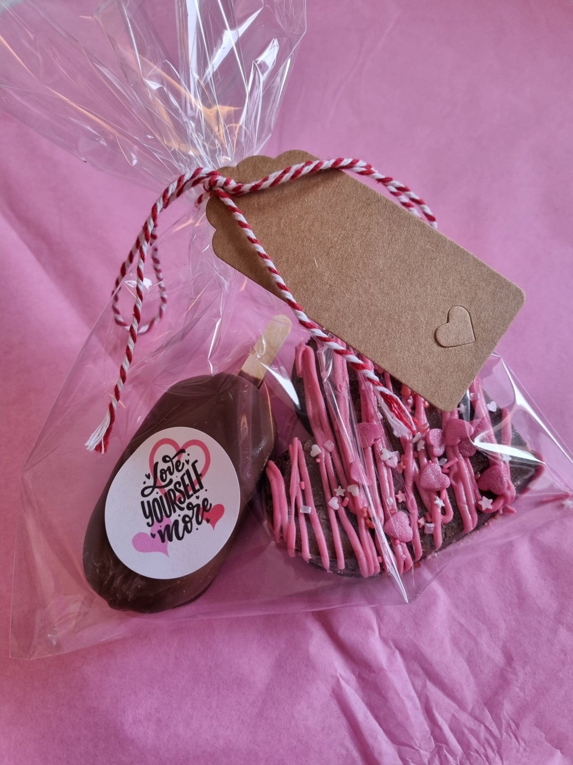 Chocolate lollipop with pink heart decorations and a tag in a cellophane bag on a pink background 
