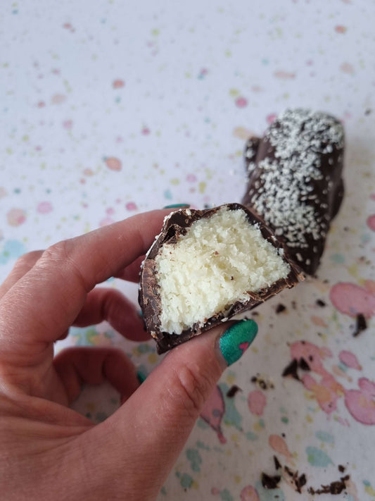 handmade Chocolate-dipped coconut treat with a white coconut filling held by a hand against a patterned background