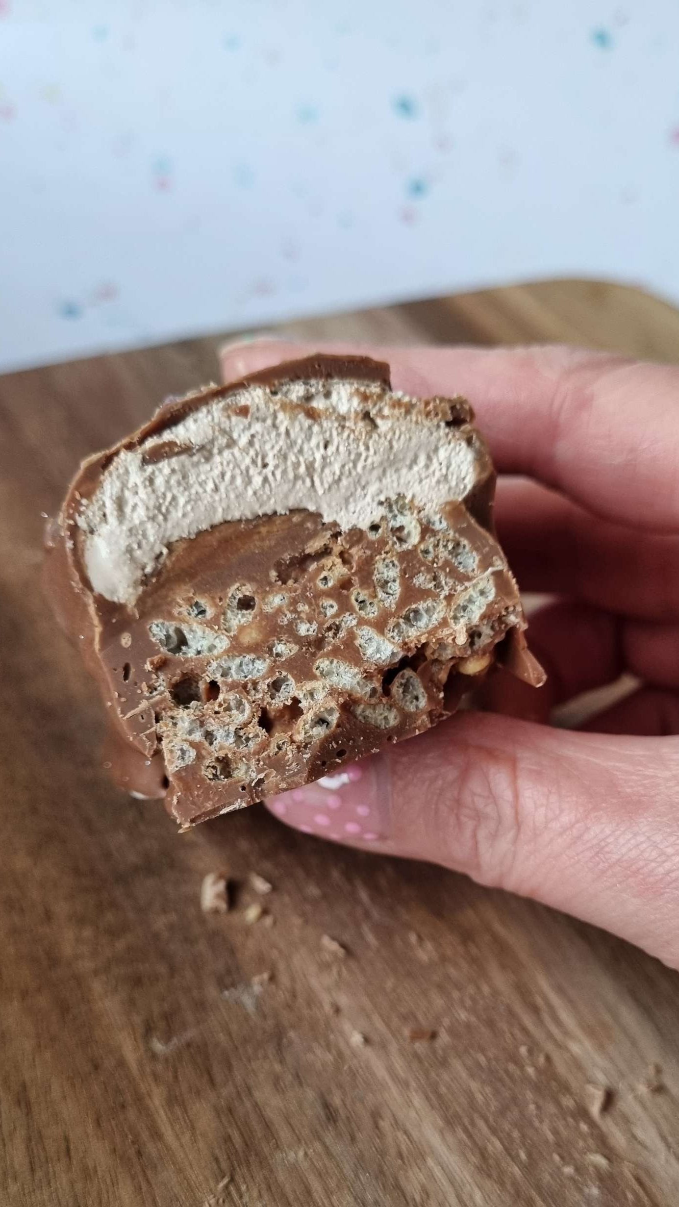 Handmade Chocolate Bar - Double Decker held by hand. layered chocolate crispies with a nougat and caramel top then all dipped in chocolate.