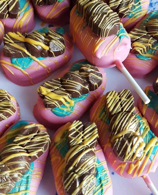 A mound of lollies on a white table. The marshmallow pops are pink and have been painted with bluey green chocolate, drizzled with yelloe chocolate and finished with a chocolate easter bunny.